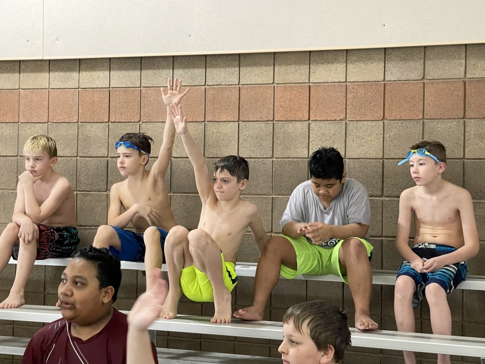 students in swimsuits sitting on pool bleachers