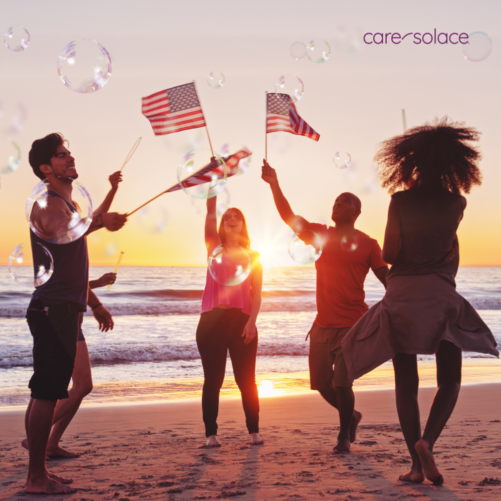 Photo of people on a beach at sunset. They are waving American flags and blowing bubbles