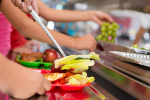 View of child's hands going through cafeteria line with food on her plate.