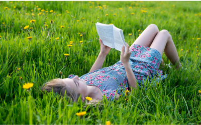 girls laying on her back in grass and reading a book