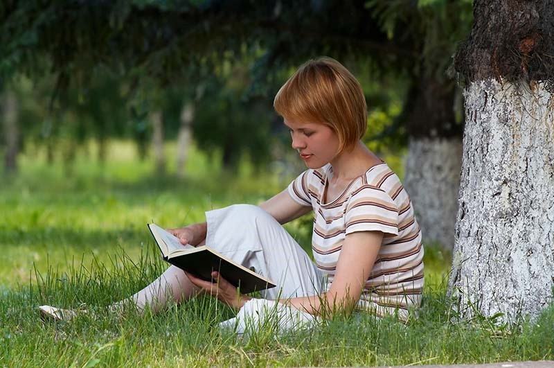 picture of girl reading a book outside under a tree